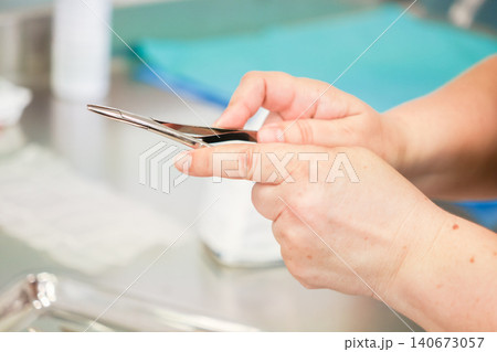 A medical professional holds a stainless steel surgical hemostat tool at a sterile clinic table, representing clinical precision and expertise during a complex surgical procedure A medical professional holds a stainless steel surgical hemostat tool at a sterile clinic table, representing clinical precision and expertise during a complex surgical procedure 140673057