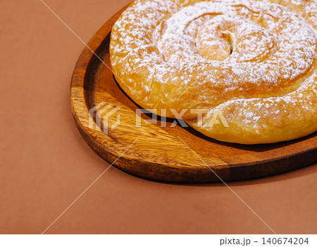 Ensaimada pastry with powdered sugar on wooden plate Ensaimada pastry with powdered sugar on wooden plate 140674204
