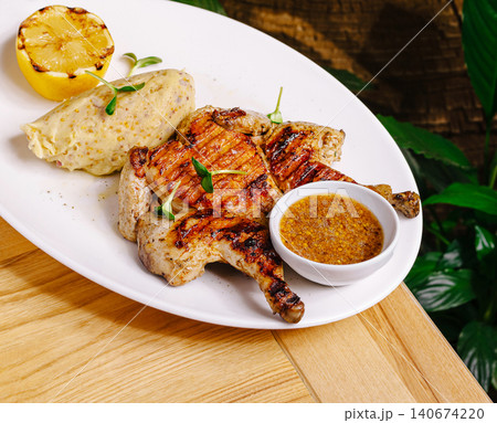 Grilled spatchcock chicken with mashed potatoes, lemon, and sauce 140674220