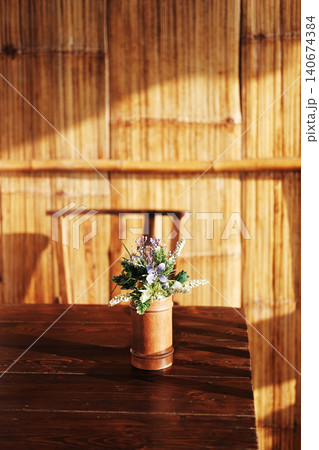 Plastic flowers in a bamboo vase decorate a wooden table in natural sunlight at the resort in Thailand Plastic flowers in a bamboo vase decorate a wooden table in natural sunlight at the resort in Thailand 140674384