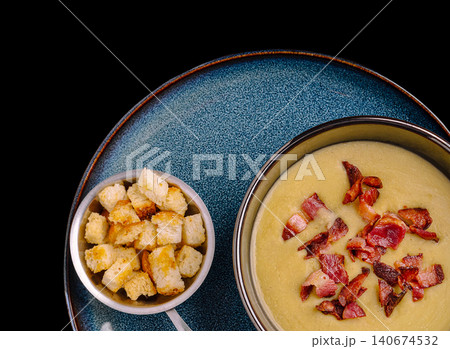 Cream soup serving with crispy bacon and croutons on blue plate 140674532