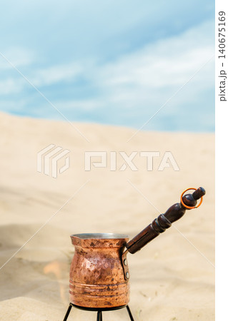 Vertical banner with a copper cezve against a sand dune and blue sky, brewing coffee using the traditional method while relaxing among the sand dunes, copy space for text Vertical banner with a copper cezve against a sand dune and blue sky, brewing coffee using the traditional method while relaxing among the sand dunes, copy space for text 140675169