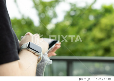 A person wearing a grey smartwatch holds a smartphone outside against a soft green park backdrop to signify constant connectivity and modern mobile lifestyle in a busy urban world A person wearing a grey smartwatch holds a smartphone outside against a soft green park backdrop to signify constant connectivity and modern mobile lifestyle in a busy urban world 140675836
