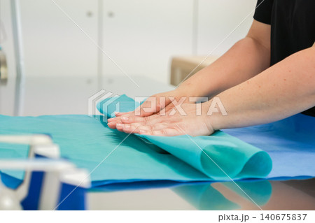 Medical professional folds sterile blue surgical drape on a metal table in a clinical setting to ensure patient safety and maintain an aseptic environment for surgery preparation Medical professional folds sterile blue surgical drape on a metal table in a clinical setting to ensure patient safety and maintain an aseptic environment for surgery preparation 140675837