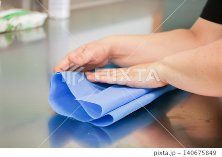 A medical professional carefully folds blue sterile nonwoven fabric on a metallic surface to illustrate essential preparation and clinical sanitation protocols in a healthcare clinic A medical professional carefully folds blue sterile nonwoven fabric on a metallic surface to illustrate essential preparation and clinical sanitation protocols in a healthcare clinic 140675849