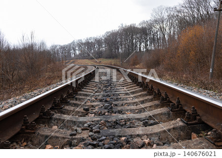 Old railway tracks stretch into the distance through a rural autumn forest landscape, symbolizing travel, journey, transportation, and paths forward toward future unknown horizons Old railway tracks stretch into the distance through a rural autumn forest landscape, symbolizing travel, journey, transportation, and paths forward toward future unknown horizons 140676021