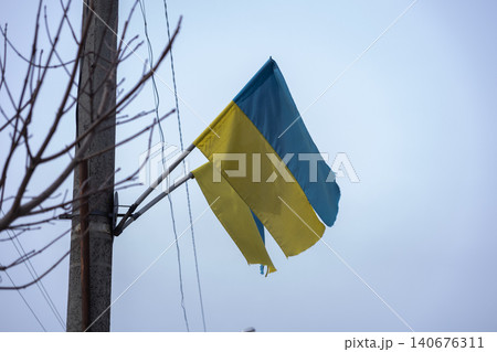 A weathered flag of Ukraine hangs from a tall utility pole against a soft gray sky, symbolizing resilience, national pride, and strength during challenging geopolitical times A weathered flag of Ukraine hangs from a tall utility pole against a soft gray sky, symbolizing resilience, national pride, and strength during challenging geopolitical times 140676311