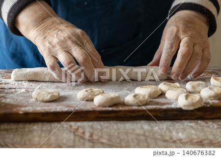 Elderly hands kneading dough for fresh homemade dumplings on a rustic wooden board, capturing the authentic tradition and warmth of preparing wholesome food in a classic kitchen setup Elderly hands kneading dough for fresh homemade dumplings on a rustic wooden board, capturing the authentic tradition and warmth of preparing wholesome food in a classic kitchen setup 140676382