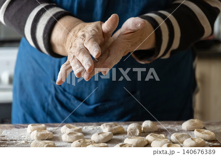 A senior person dusts flour off hands while preparing handmade dumplings on a wooden board, showcasing traditional culinary skills and a warm, authentic home kitchen cooking atmosphere A senior person dusts flour off hands while preparing handmade dumplings on a wooden board, showcasing traditional culinary skills and a warm, authentic home kitchen cooking atmosphere 140676389