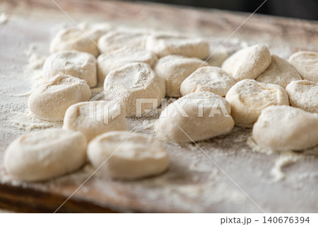 Fresh dough balls for handmade dumplings rest on a flour-dusted wooden board, capturing the authentic artisanal process of preparing traditional homemade savory pastry appetizers meal Fresh dough balls for handmade dumplings rest on a flour-dusted wooden board, capturing the authentic artisanal process of preparing traditional homemade savory pastry appetizers meal 140676394