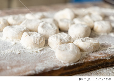 Fresh handmade dumplings arranged on a rustic wooden board dusted with wheat flour for culinary preparation, representing authentic artisan cooking traditions in a home kitchen setting Fresh handmade dumplings arranged on a rustic wooden board dusted with wheat flour for culinary preparation, representing authentic artisan cooking traditions in a home kitchen setting 140676396