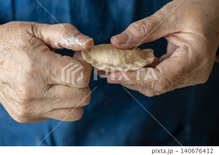 Senior person folding a fresh homemade dumpling with floured hands in a kitchen, representing authentic culinary traditions and the warmth of preparing a healthy meal for family home Senior person folding a fresh homemade dumpling with floured hands in a kitchen, representing authentic culinary traditions and the warmth of preparing a healthy meal for family home 140676412