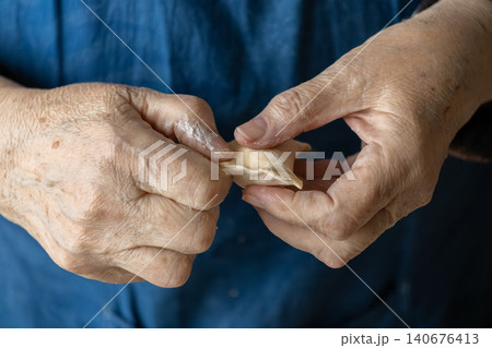An elderly person carefully shapes a fresh handmade dumpling with floured hands, representing traditional culinary craftsmanship, wholesome home cooking, and authentic heritage food 140676413