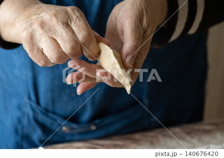 Elderly person pinching edges of a fresh raw dumpling dough piece by hand, capturing a traditional culinary technique for making authentic homemade food in a cozy kitchen setting Elderly person pinching edges of a fresh raw dumpling dough piece by hand, capturing a traditional culinary technique for making authentic homemade food in a cozy kitchen setting 140676420