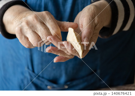 A senior person carefully shaping a handmade dumpling with floured hands in a kitchen, representing authentic traditional cooking techniques and a nostalgic homemade meal atmosphere 140676421