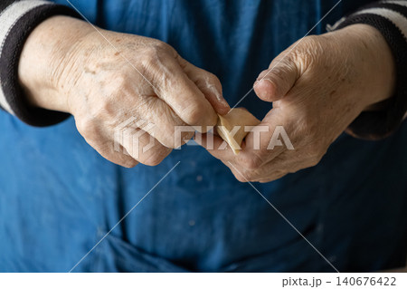 Elderly hands carefully shaping a dough dumpling in a home kitchen, highlighting the skilled preparation of traditional handmade cuisine with love and attention to fine culinary detail Elderly hands carefully shaping a dough dumpling in a home kitchen, highlighting the skilled preparation of traditional handmade cuisine with love and attention to fine culinary detail 140676422
