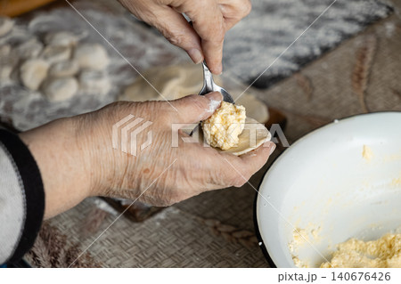 Elderly person preparing handmade dumplings by placing filling onto dough circles on a wooden table, emphasizing traditional culinary skills in a warm home kitchen environment setting Elderly person preparing handmade dumplings by placing filling onto dough circles on a wooden table, emphasizing traditional culinary skills in a warm home kitchen environment setting 140676426