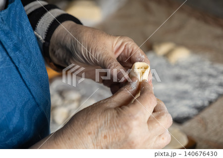 A senior person carefully shaping a dough dumpling by hand in a rustic kitchen, highlighting traditional culinary techniques, homemade food preparation and authentic domestic heritage A senior person carefully shaping a dough dumpling by hand in a rustic kitchen, highlighting traditional culinary techniques, homemade food preparation and authentic domestic heritage 140676430