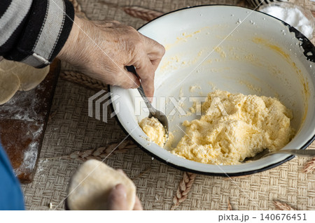 A senior person fills raw dough for homemade dumplings using a spoon in a rustic kitchen setting, capturing the traditional process of creating authentic food with fresh ingredients A senior person fills raw dough for homemade dumplings using a spoon in a rustic kitchen setting, capturing the traditional process of creating authentic food with fresh ingredients 140676451