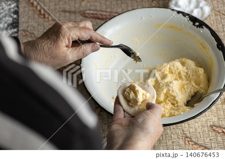 An elderly person carefully spoons creamy filling onto a round dough disc to prepare homemade dumplings, highlighting traditional culinary techniques and classic family cooking An elderly person carefully spoons creamy filling onto a round dough disc to prepare homemade dumplings, highlighting traditional culinary techniques and classic family cooking 140676453