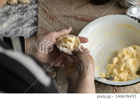 An elderly person carefully shapes dough with cheese filling to prepare traditional dumplings, emphasizing culinary craft and heritage in a cozy rustic home kitchen setting today 140676455