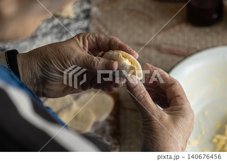 Elderly person hand folds a homemade dumpling filled with cottage cheese, capturing an authentic culinary tradition in a rustic kitchen setting to celebrate slow food and heritage Elderly person hand folds a homemade dumpling filled with cottage cheese, capturing an authentic culinary tradition in a rustic kitchen setting to celebrate slow food and heritage 140676456