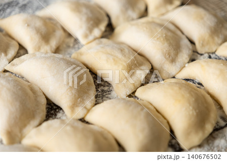 Raw homemade dumplings arranged neatly on a dusted surface before cooking to display artisanal preparation for authentic culinary traditions during festive family mealtime kitchen work Raw homemade dumplings arranged neatly on a dusted surface before cooking to display artisanal preparation for authentic culinary traditions during festive family mealtime kitchen work 140676502