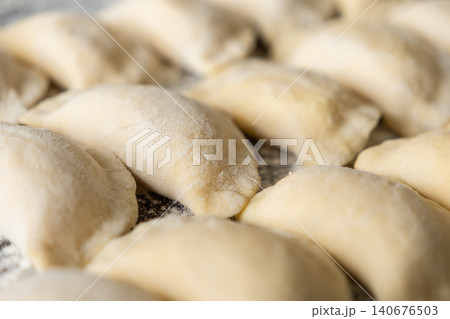 Fresh handmade dumplings arranged in rows on a floured surface for cooking, highlighting culinary preparation, artisanal food craftsmanship, and the traditional process of home dining Fresh handmade dumplings arranged in rows on a floured surface for cooking, highlighting culinary preparation, artisanal food craftsmanship, and the traditional process of home dining 140676503