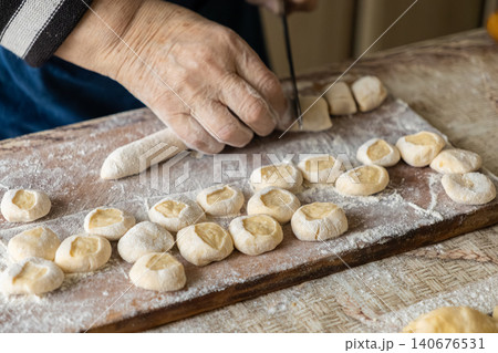 Elderly hands cutting dough pieces for dumplings on a floured wooden board, representing home cooking, traditional culinary heritage, skilled manual craft and authentic food preparation Elderly hands cutting dough pieces for dumplings on a floured wooden board, representing home cooking, traditional culinary heritage, skilled manual craft and authentic food preparation 140676531