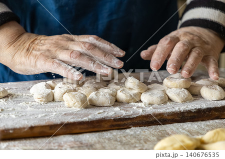 A senior person dusts raw homemade dumplings with flour on a wooden board for cooking, highlighting traditional culinary preparation and authentic handcrafted meal creation at home A senior person dusts raw homemade dumplings with flour on a wooden board for cooking, highlighting traditional culinary preparation and authentic handcrafted meal creation at home 140676535