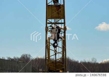 A construction crane stands tall at a building site. It lifts materials into the air while workers move around 140676598