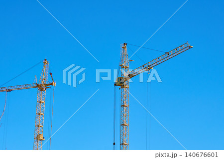 Construction crane stands tall against the blue sky during the day in an urban area Construction crane stands tall against the blue sky during the day in an urban area 140676601