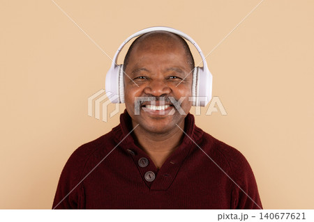 African American man in burgundy sweater smiling while wearing white wireless headphones African American man in burgundy sweater smiling while wearing white wireless headphones 140677621