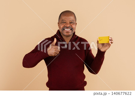 Smiling mature black man holding yellow credit card and showing thumbs up Smiling mature black man holding yellow credit card and showing thumbs up 140677622