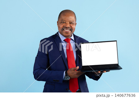 Smiling mature black businessman in suit holding open laptop with blank screen Smiling mature black businessman in suit holding open laptop with blank screen 140677636