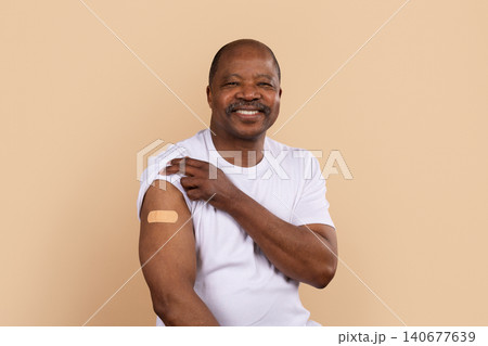 Mature black man in white shirt showing bandage on arm after vaccination Mature black man in white shirt showing bandage on arm after vaccination 140677639