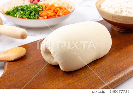 Fresh raw wheat dough on wooden cutting board for making traditional Chinese dumplings Fresh raw wheat dough on wooden cutting board for making traditional Chinese dumplings 140677725