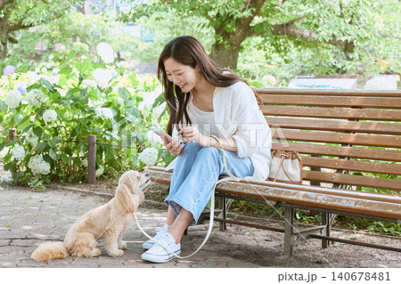 公園のベンチでスマホを持ち愛犬と微笑む若い女性 公園のベンチでスマホを持ち愛犬と微笑む若い女性 140678481