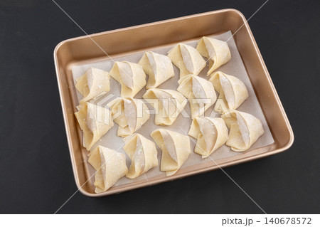 Freshly made wonton wrappers are arranged on a tray, along with uncooked dumplings. 140678572