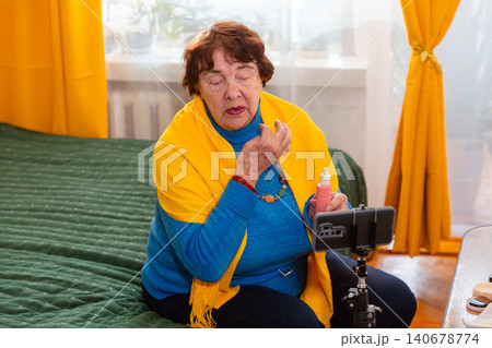 Caucasian grandmother creating beauty related content while reviewing personal care products. Influencer concept. Comfortable indoor environment and retirement. Mid shot 140678774