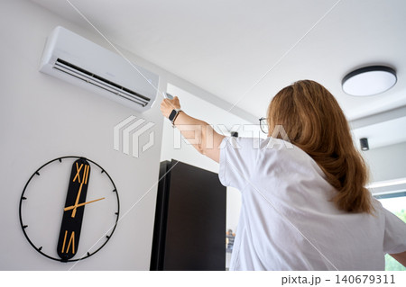 Woman turning on air conditioner with remote control Woman turning on air conditioner with remote control 140679311