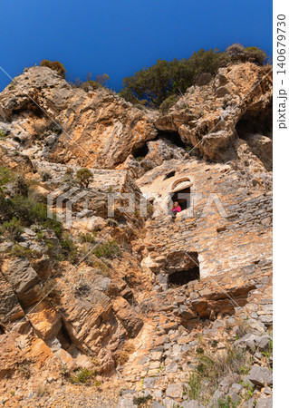 Woman looking at beautiful view from window of Afkule monastery carved into high vertical cliffs near Oludeniz, Turkey. Dramatic rock landscape and historic architecture. Travel, cultural destination. Woman looking at beautiful view from window of Afkule monastery carved into high vertical cliffs near Oludeniz, Turkey. Dramatic rock landscape and historic architecture. Travel, cultural destination. 140679730