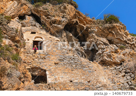 Woman looking at beautiful view from window of Afkule monastery carved into high vertical cliffs near Oludeniz, Turkey. Dramatic rock landscape and historic architecture. Travel, cultural destination. Woman looking at beautiful view from window of Afkule monastery carved into high vertical cliffs near Oludeniz, Turkey. Dramatic rock landscape and historic architecture. Travel, cultural destination. 140679733
