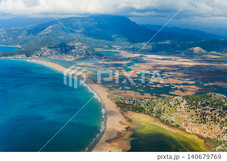 Aerial view of Iztuzu Beach and Dalyan river delta in Mugla, Turkey. Long sandy coastline, lagoon and mountains create a perfect destination for summer family travel, hiking and nature tourism. Aerial view of Iztuzu Beach and Dalyan river delta in Mugla, Turkey. Long sandy coastline, lagoon and mountains create a perfect destination for summer family travel, hiking and nature tourism. 140679769