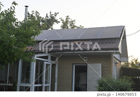 Modern home with solar panels on roof, surrounded by greenery. 140679853