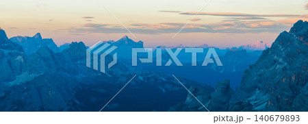 Wide panoramic view of the Dolomites during blue hour featuring distant mountain ranges, soft pastel colors and tranquil alpine scenery in northern Italy. 140679893