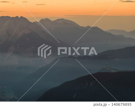 Warm orange sunset illuminates the dramatic peaks and valleys of the Dolomites, creating an atmospheric alpine landscape with layered mountain silhouettes in Italy. Warm orange sunset illuminates the dramatic peaks and valleys of the Dolomites, creating an atmospheric alpine landscape with layered mountain silhouettes in Italy. 140679895