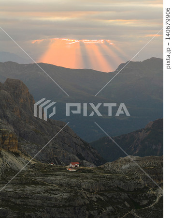 Powerful sunbeams break through dramatic storm clouds above the Tre Cime di Lavaredo region in the Dolomites, Italy. Aerial view of rugged alpine terrain illuminated by golden evening light. Powerful sunbeams break through dramatic storm clouds above the Tre Cime di Lavaredo region in the Dolomites, Italy. Aerial view of rugged alpine terrain illuminated by golden evening light. 140679906