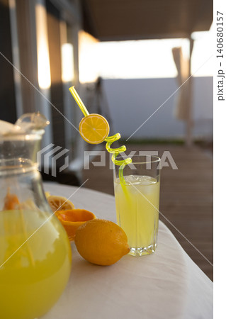 Glass of fresh lemonade with lemons and curvy straw on outdoor table at sunset Glass of fresh lemonade with lemons and curvy straw on outdoor table at sunset 140680157