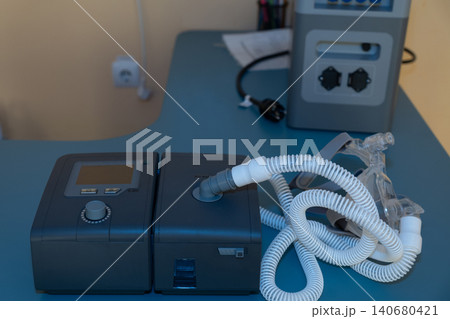 Medical CPAP machine with tubing and mask on blue surface in clinical setting for sleep apnea treatment. Medical CPAP machine with tubing and mask on blue surface in clinical setting for sleep apnea treatment. 140680421